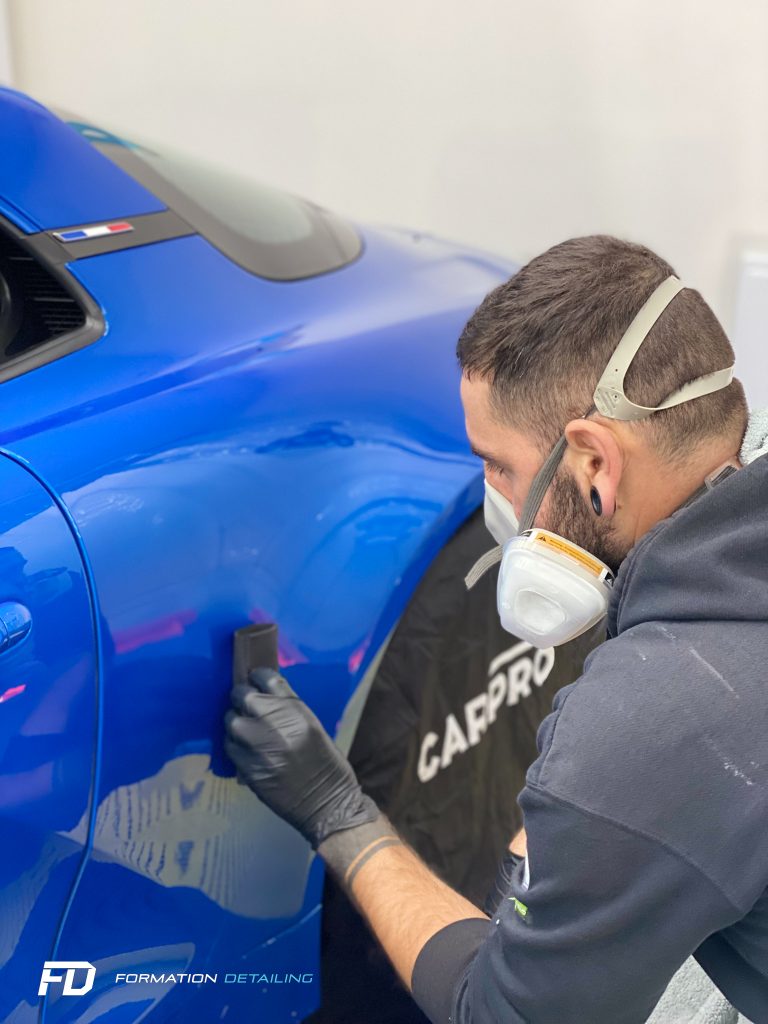 Stagiaire en formation detailing intervenant sur la carrosserie d’un véhicule bleu